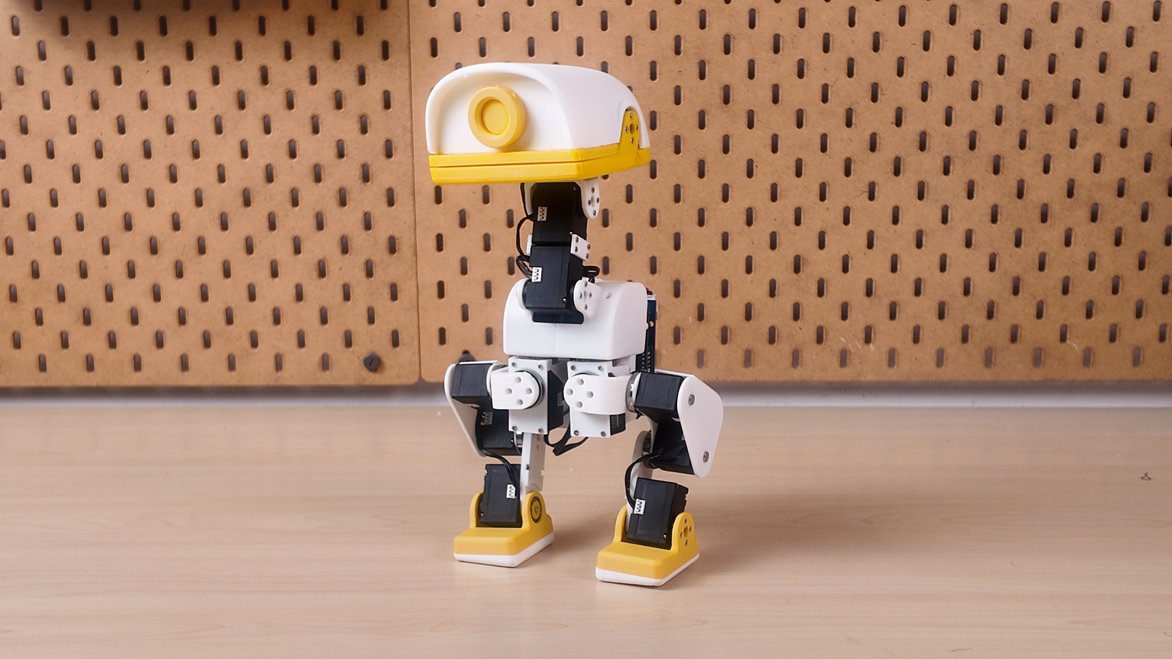 XGO-Duck standing on a workbench, with a white printed body, yellow beak and feet, and exposed leg joints