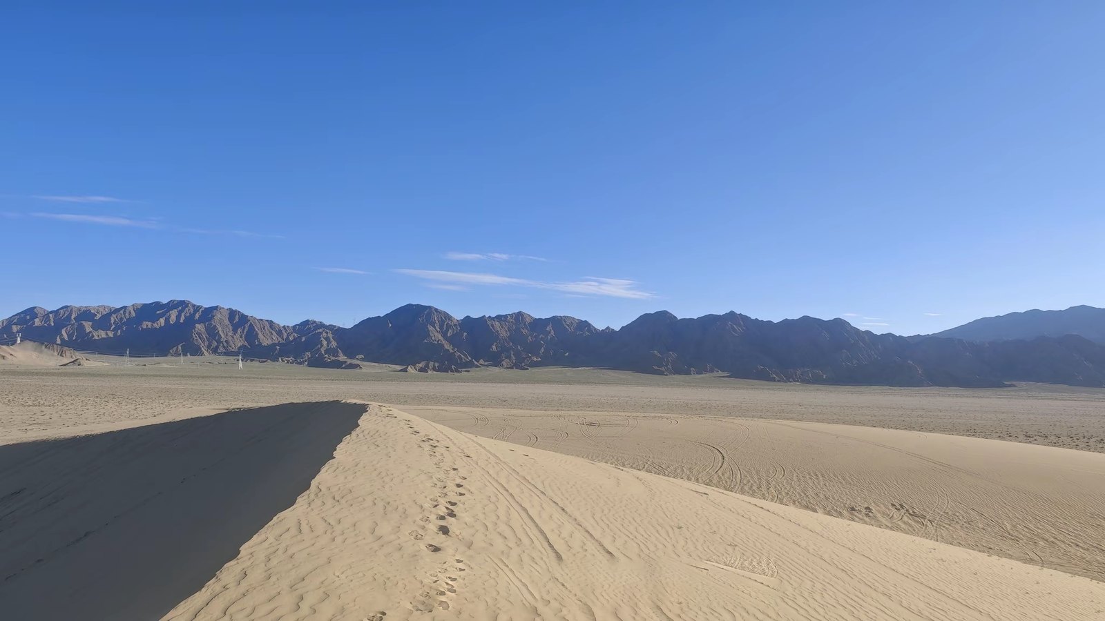 The photo: a sand dune ridge, bare dark mountains, pylons at the foot of the range
